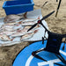 A black AEE Condor Pro Fishing Drone with red accents is shown on a sandy beach next to several caught Snapper fish laid out on a white towel and a blue landing pad. A blue storage bin is visible in the background.