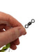 A close-up of a hand holding a small black swiveling snap hook with a clear fishing line and light-colored fly hair against a plain white background.